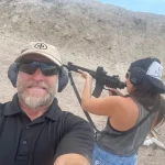 Gun trainer smiling with student in background shooting AR15